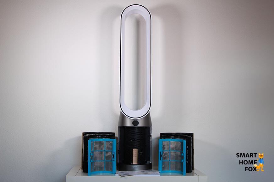 Der Dyson Purifier Cool steht auf einem Regal, daneben liegen die Filtereinheiten, die Fernbedienung und die Anleitung.